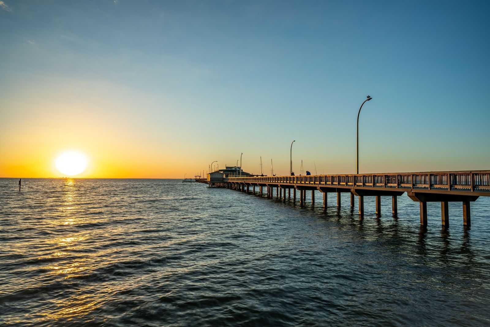 The sun setting beside the Fairhope Municipal Pier on Mobile Bay, with lamp posts along the pier